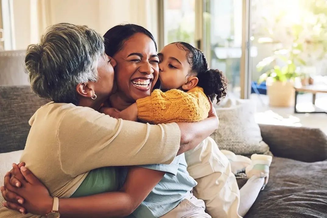 a woman is embraced lovingly by her mother and her daughter.