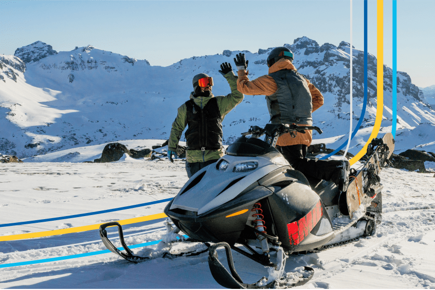 two people high-five beside a snowmobile