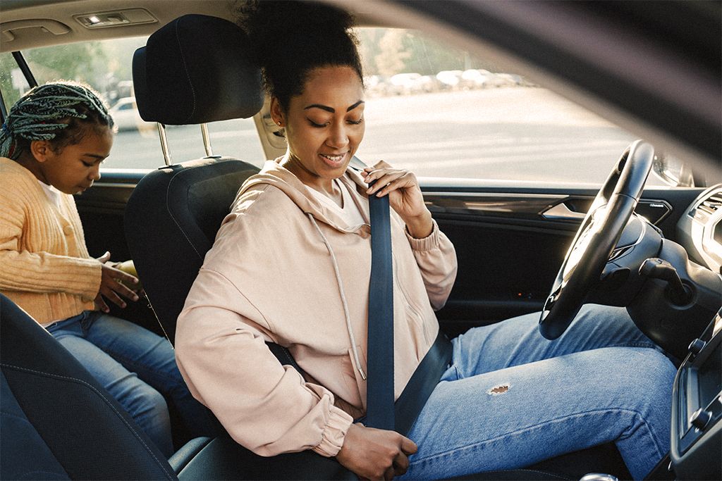 Black woman smiling and wearing seat belt while sitting with her daughter in car