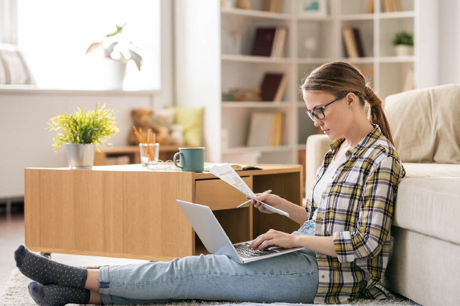Une femme regardant un écran d'ordinateur portable et tenant du papier.