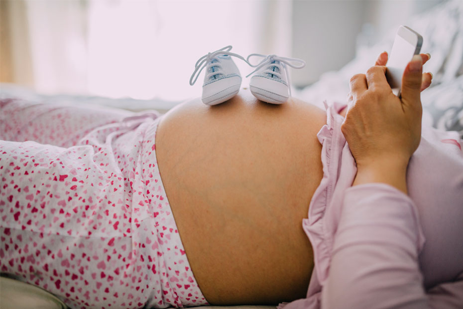 Femme enceinte sur son téléphone, et réfléchissant à la façon de se préparer à l'arrivée du bébé.